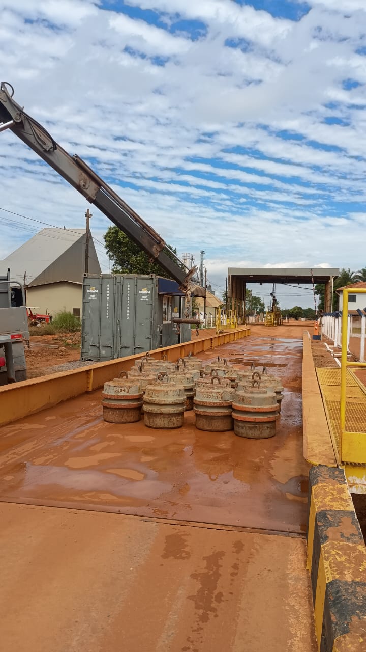 Pesos padrão sobre balança rodoviária com guindaste e cabine de pesagem ao fundo